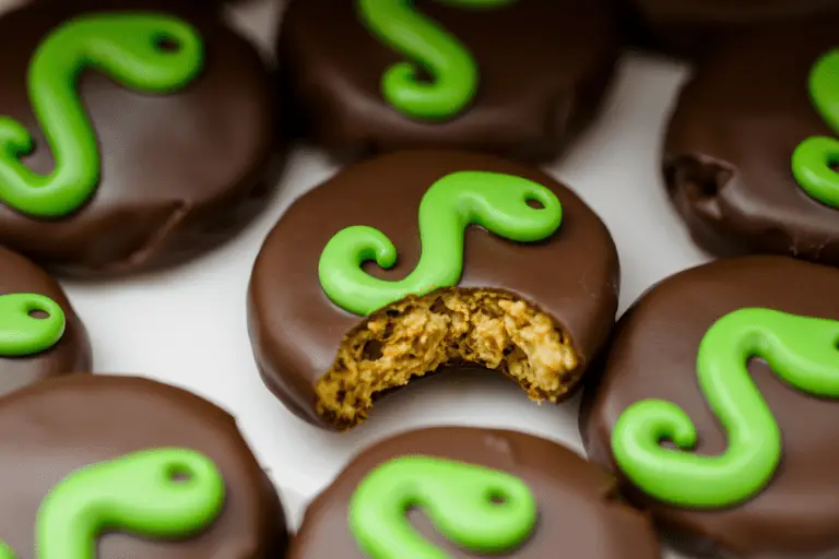 A set of chocolate-covered cookies with green snake-shaped icing designs, arranged on a dark surface. One cookie has a bite taken out, showing a golden-brown, crumbly interior. The setting has a moody, magical feel, with soft lighting adding a mystical touch.