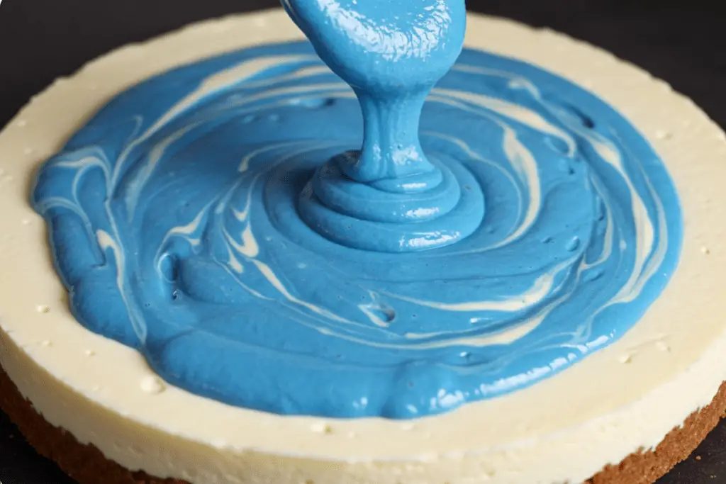 Blue velvet batter being swirled into the cheesecake layer to create a stunning marbled effect resembling a starry sky.