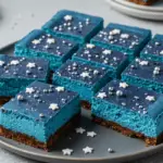 Starry Sky Blue Velvet Cheesecake Bars with a rich blue velvet cheesecake layer, graham cracker crust, and edible gold stars, set in a magical, celestial-themed setting with blueberries and soft lighting.