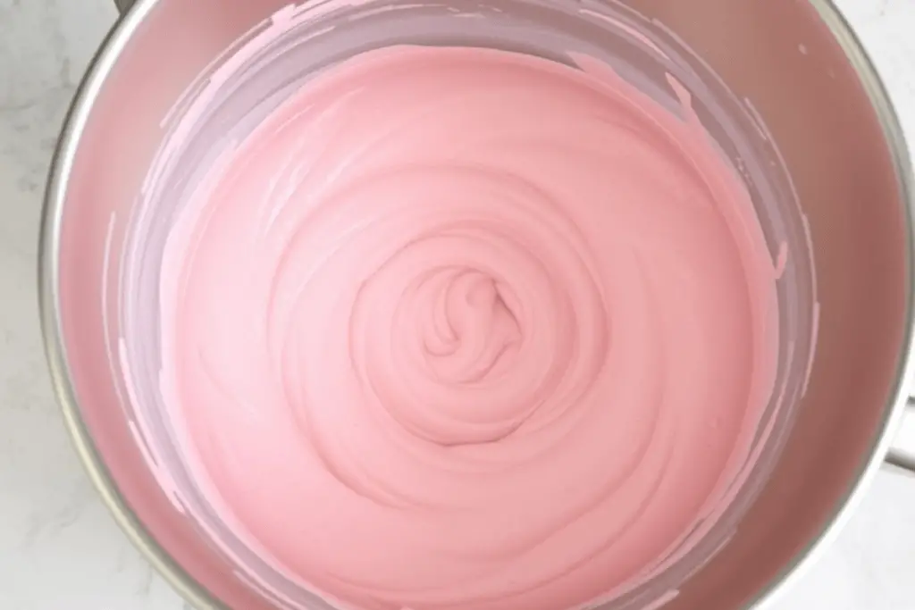 A mixing bowl filled with pink strawberry cheesecake batter, being folded until smooth and creamy.