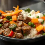 A plate of rice and cubed beef with steamed vegetables, an affordable, healthy meal.